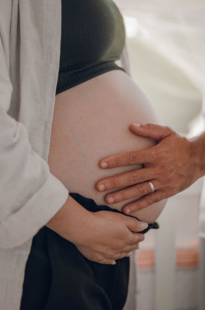 A pregnant woman is tenderly touching her belly with a man's supportive hand.