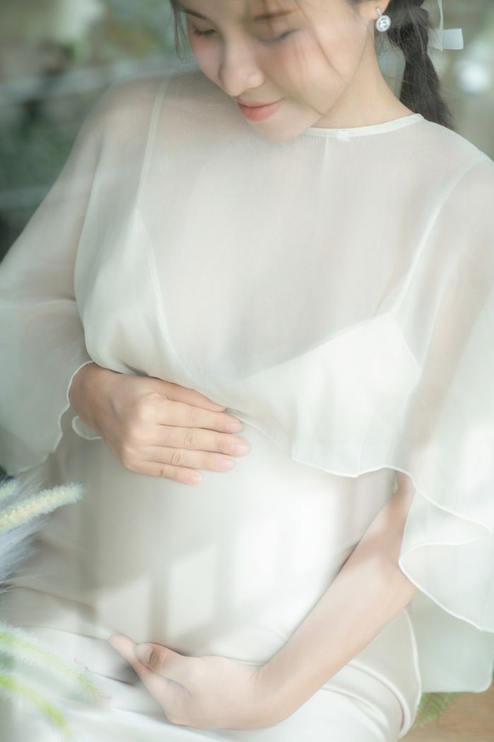 Serene image of a pregnant woman gently holding her belly in soft light.