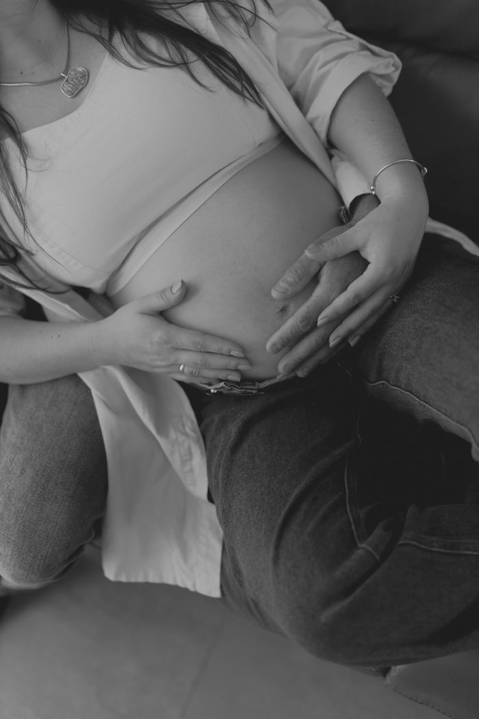 Intimate black and white photo of a pregnant couple gently holding the baby bump.
