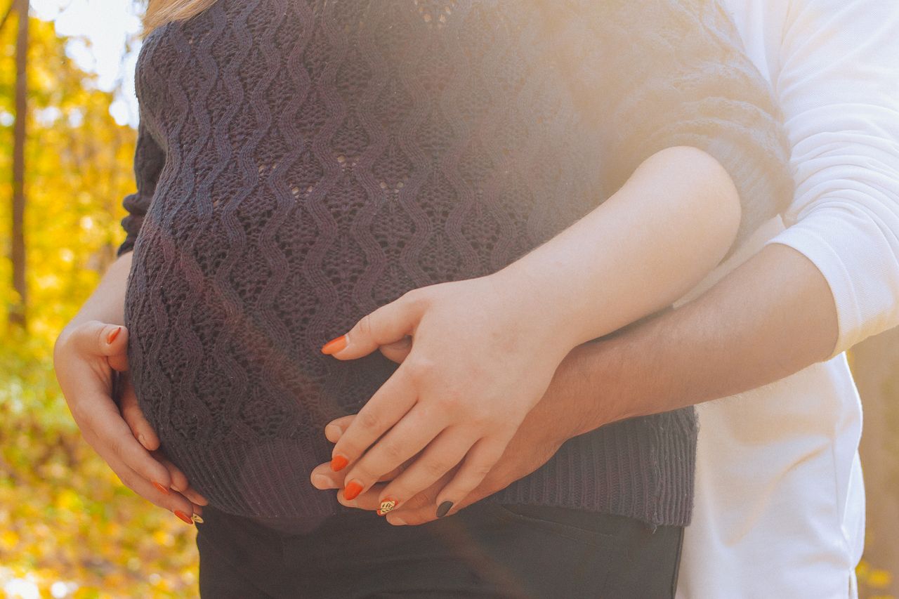 A warm, intimate moment of a couple embracing, highlighting a pregnant belly in sunlight.